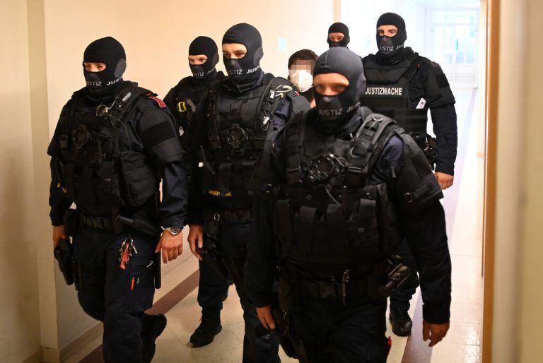 Polizeibeamte führen einen der Angeklagten zum Gerichtssaal. apa