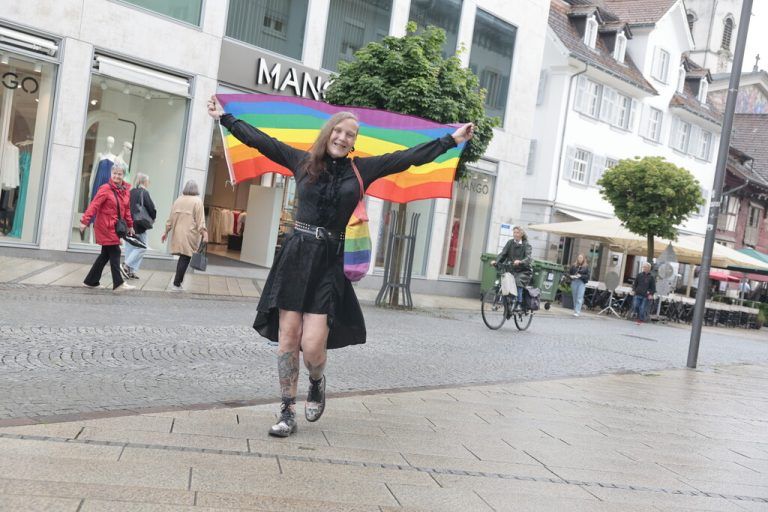 Mit ihrem Outfit und der Regenbogenflagge – ein Zeichen der queeren Community – zieht sie Blicke in Dornbirn auf sich.