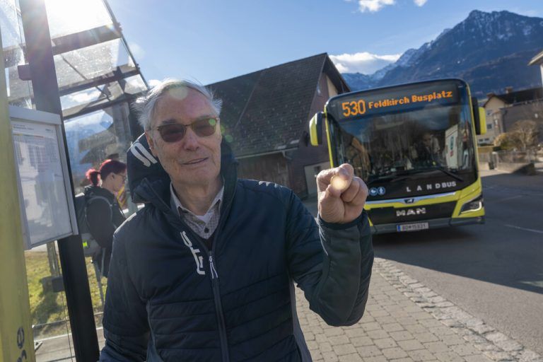Günther Mähr an einer Bushaltestelle in Satteins. Symbolisch für die Preiserhöhung hält er ein 50-Cent-Stück in die Höhe.⇒hartinger
