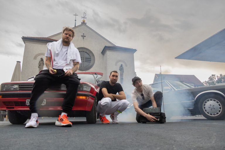 Johannes Maas (l.), Kerim El-Mokdad und Ali Europa mit ihren Autos auf dem Kirchplatz in Lustenau.⇒Hartinger