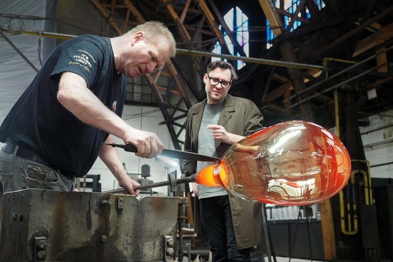 Ein Handwerker der Glashütte Lamperts (l.) formt die Auftragsarbeit in Anwesenheit des Künstlers. ⇒Egger